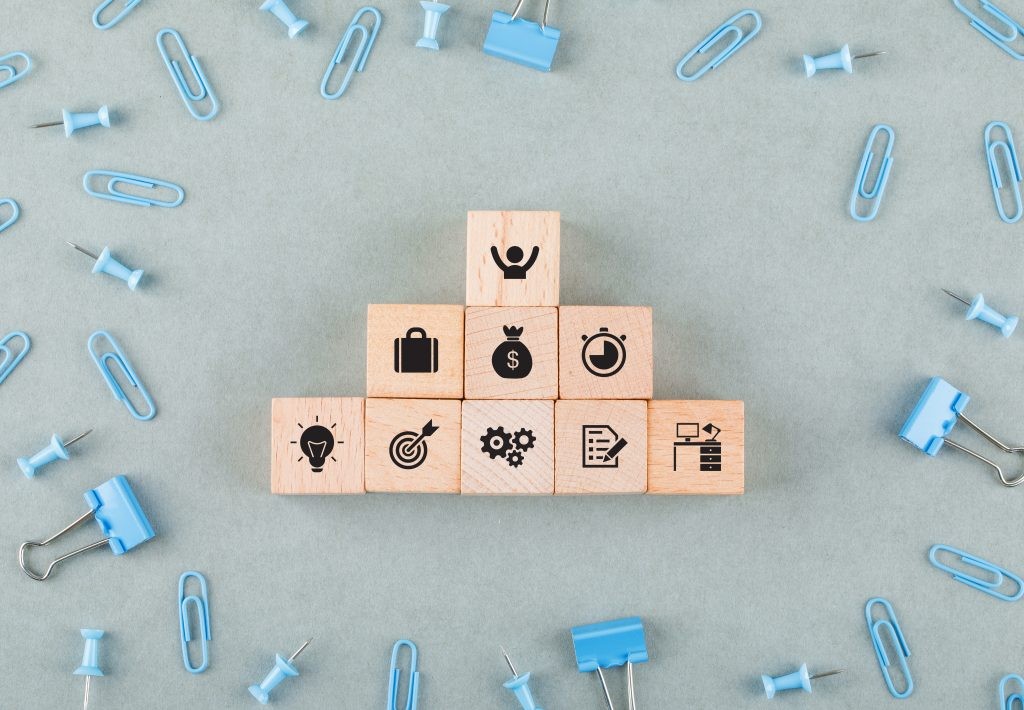 Conceptual of business office with wooden blocks with icons, paperclips, binder clips on sage color background top view. horizontal image